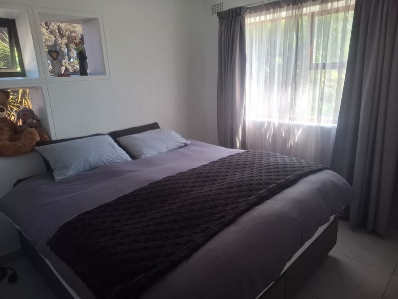 A comfortable bedroom featuring a built-in wall niche for storage and a large window with curtains allowing natural light.