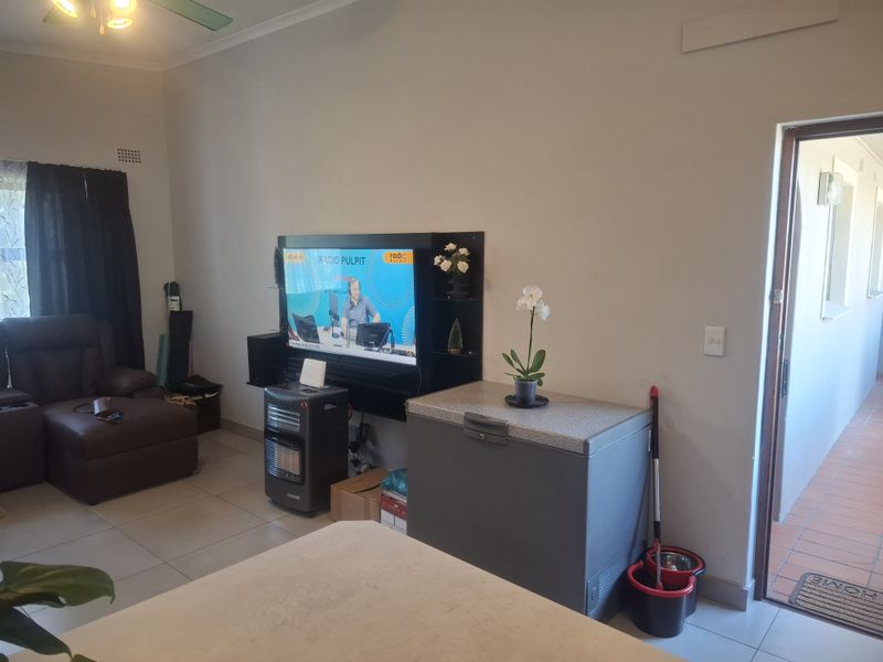 A living room area featuring tiled flooring, a ceiling fan, and a wall-mounted television unit, providing a functional space for relaxation.