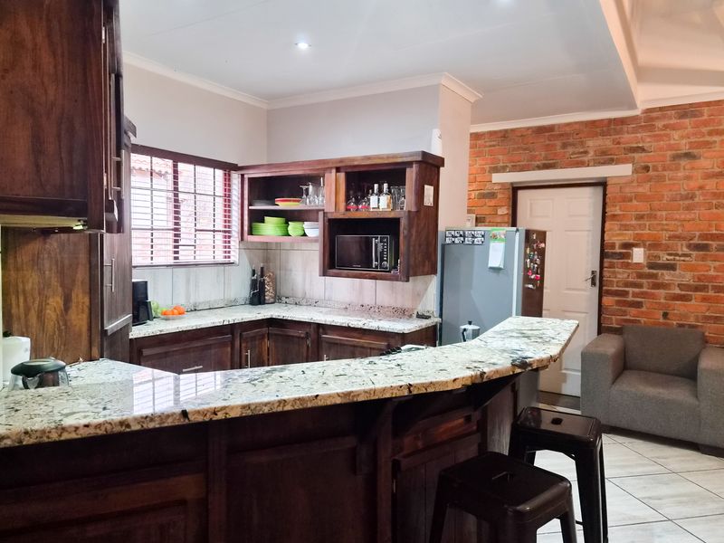 A functional kitchen featuring dark wood cabinetry, granite countertops with a breakfast bar, and a rustic exposed brick feature wall.