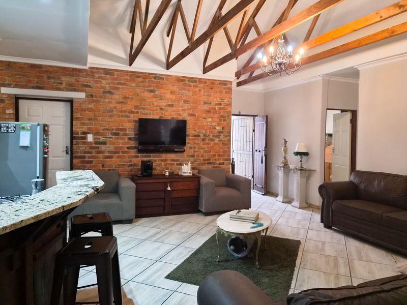 Spacious open-plan living area featuring a striking exposed brick wall, vaulted ceilings with timber trusses, and a granite breakfast bar.