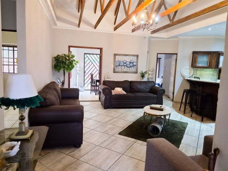 Open-plan living area featuring high vaulted ceilings with exposed timber trusses, tiled flooring, and a breakfast bar connecting to the kitchen space.