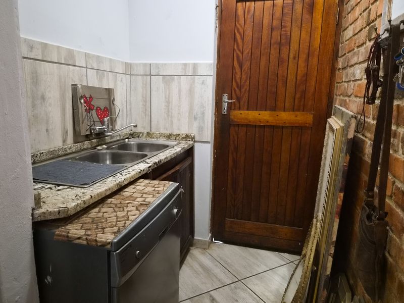 Compact scullery area featuring a double sink, granite countertops, tiled backsplash, and a rustic exposed brick wall with a wooden door.