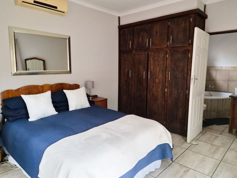 Bedroom featuring built-in wooden cupboards, tiled flooring, and an integrated air conditioning unit, with direct access to an en-suite bathroom.