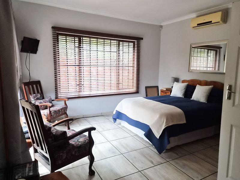A bedroom featuring tiled flooring, an installed air conditioning unit, and large windows with venetian blinds.