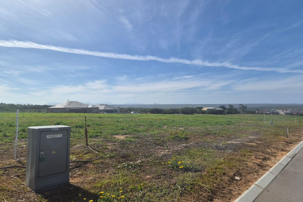 A vacant residential plot featuring a clear view of the surrounding landscape, accessible via a paved road with an existing electrical connection point.