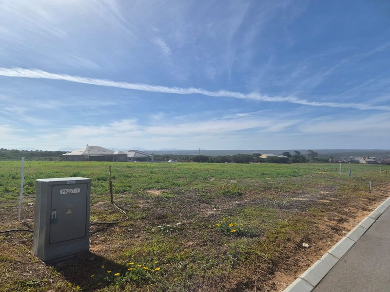 A vacant residential plot featuring a clear view of the surrounding landscape, accessible via a paved road with an existing electrical connection point.