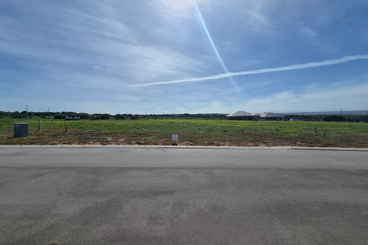 A street-level view of a vacant residential plot featuring paved road access and clear sightlines to the surrounding landscape.