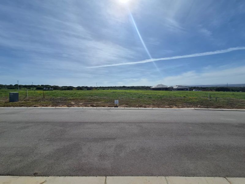 A street-level view of a vacant residential plot featuring paved road access and clear sightlines to the surrounding landscape.