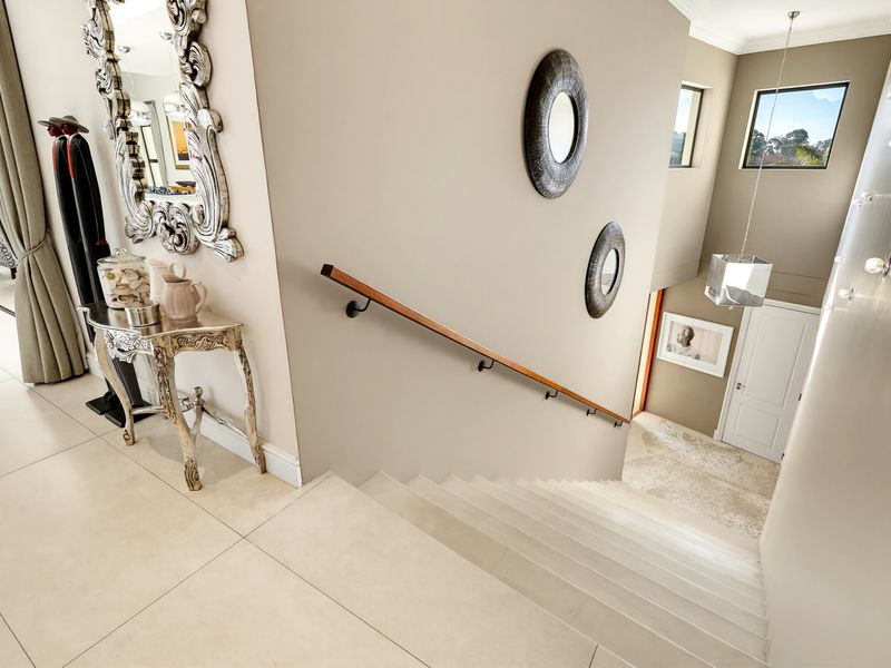 A bright and modern hallway featuring a staircase with a wooden handrail, large format floor tiles, and contemporary lighting fixtures.