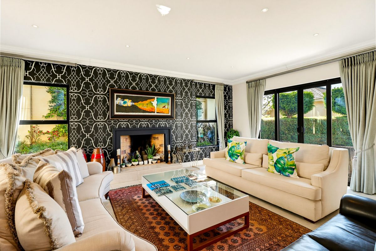 A well-lit living room featuring a prominent fireplace with decorative wallpaper, recessed ceiling lights, and large sliding glass doors providing access to the garden.