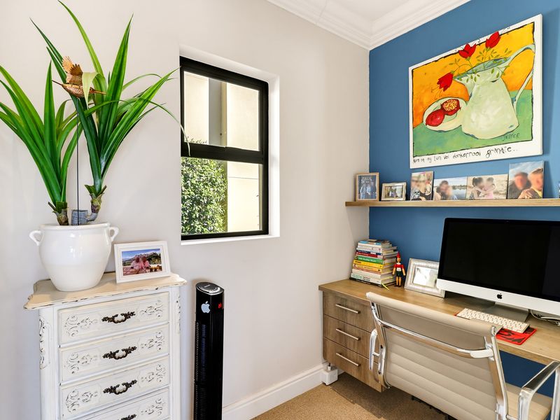 A functional home office featuring a built-in desk, floating shelving, and a modern black-framed window with a feature wall.
