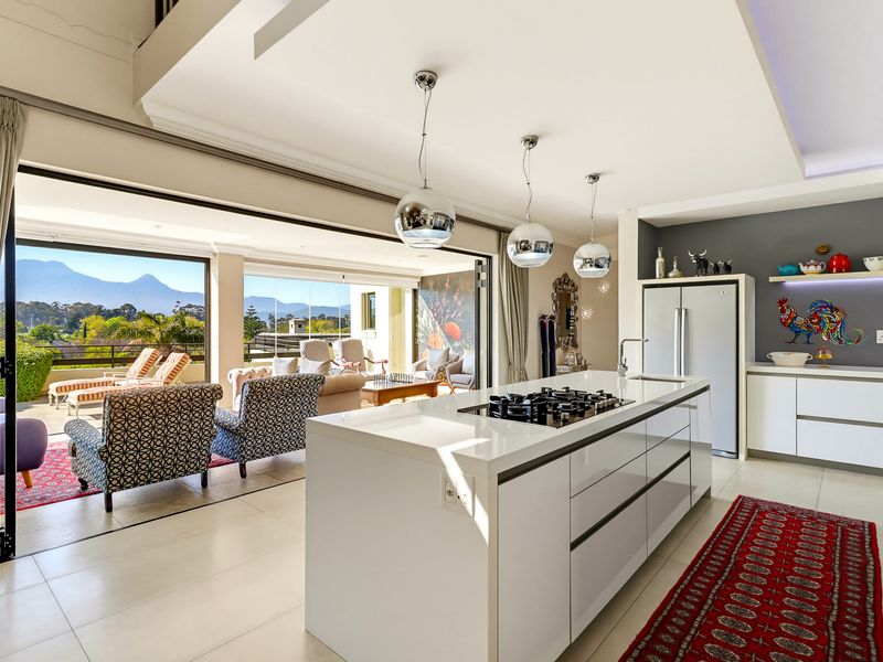 Modern open-plan kitchen and living area featuring a central island with gas cooktop, sleek cabinetry, and seamless flow to a spacious outdoor balcony.