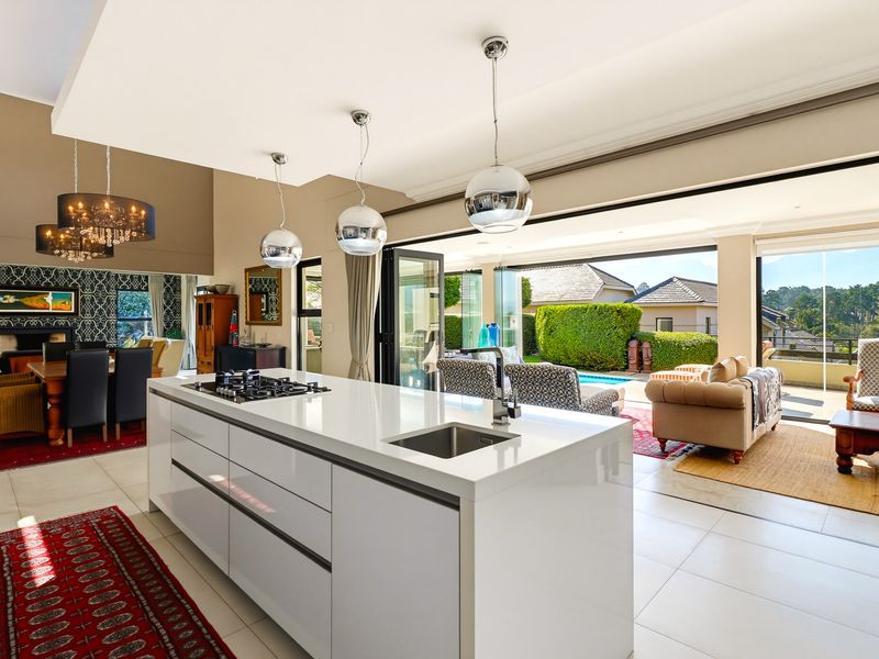 Spacious open-plan kitchen and living area featuring a modern island, sleek cabinetry, and seamless indoor-outdoor flow through large bi-fold doors to the patio.