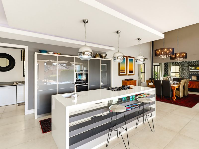 Modern open-plan kitchen featuring a large central island with gas hob, sleek cabinetry, and integrated appliances, flowing into a spacious dining and living area.