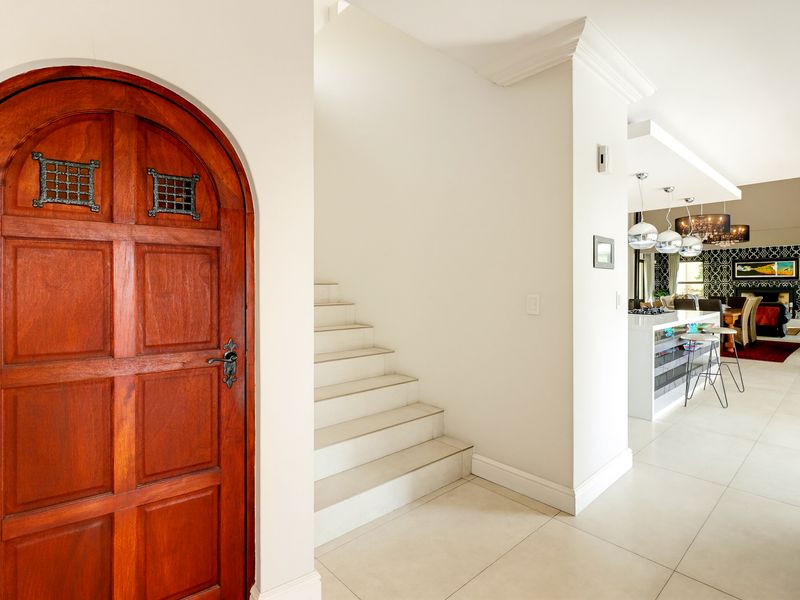 Welcoming entrance hall featuring an arched wooden door, tiled staircase, and seamless flow into the open-plan kitchen and living area.