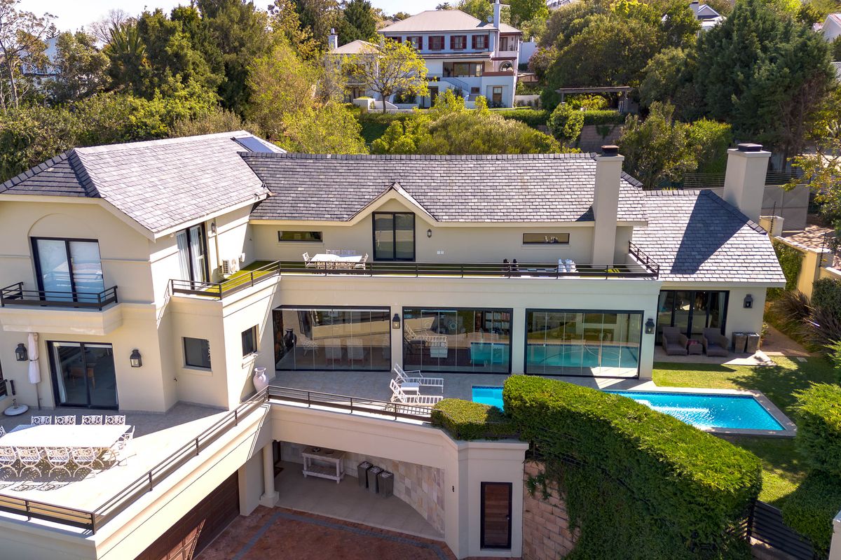 Aerial view of a multi-level luxury residence featuring a slate roof, expansive balconies, a swimming pool, and integrated patio areas.