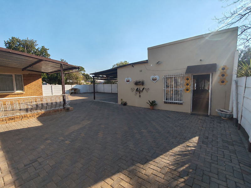 Rear exterior view featuring a paved courtyard, covered patio area, and secure boundary walling.