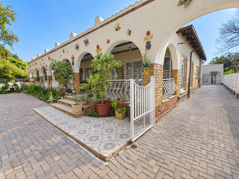 A covered patio area featuring distinctive arched architecture, brick detailing, and paved flooring, providing a sheltered outdoor space along the side of the house.