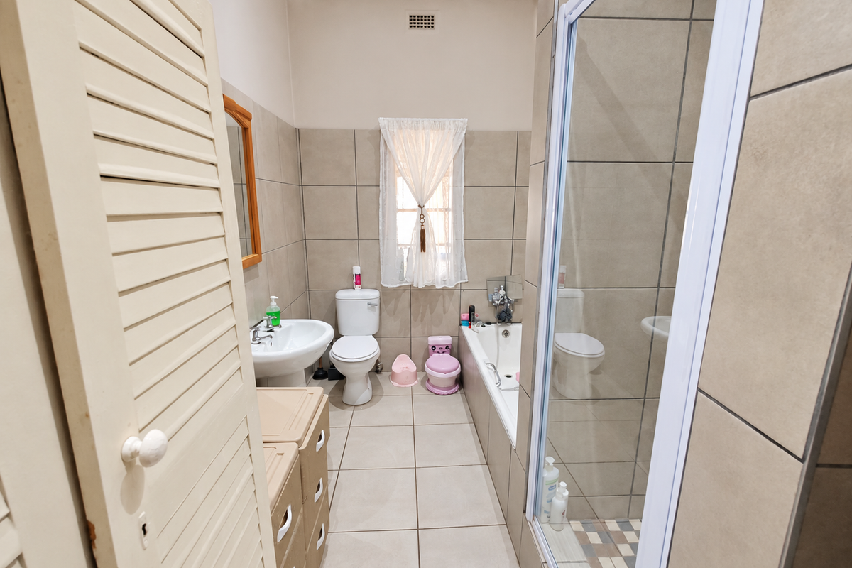 A functional bathroom featuring a pedestal basin, toilet, bathtub, and a separate shower enclosure with neutral wall and floor tiling.