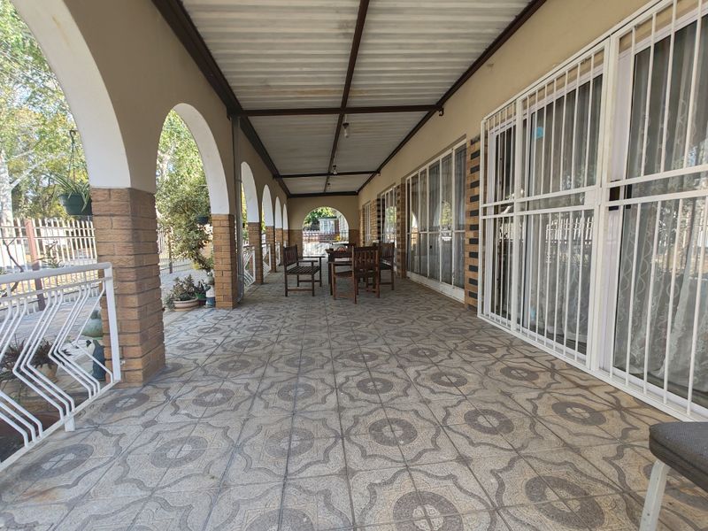 A covered patio area featuring arched brick columns, patterned floor tiles, and secure sliding glass door access to the home interior.