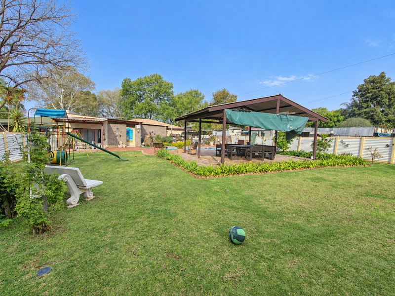 Spacious rear garden featuring a large lawn, a covered patio entertainment area, and a swimming pool, providing an ideal space for outdoor living.