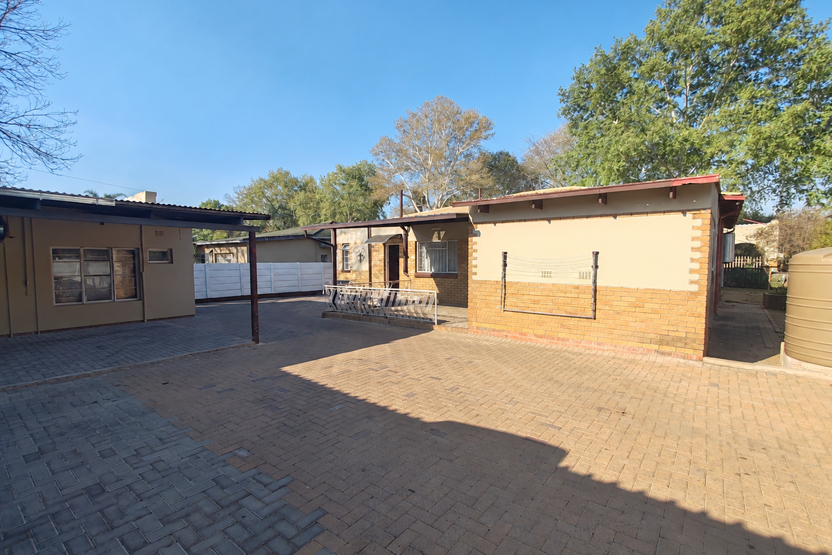 Rear exterior view of the property featuring a large paved courtyard, covered patio area, brick facade, and a water storage tank.