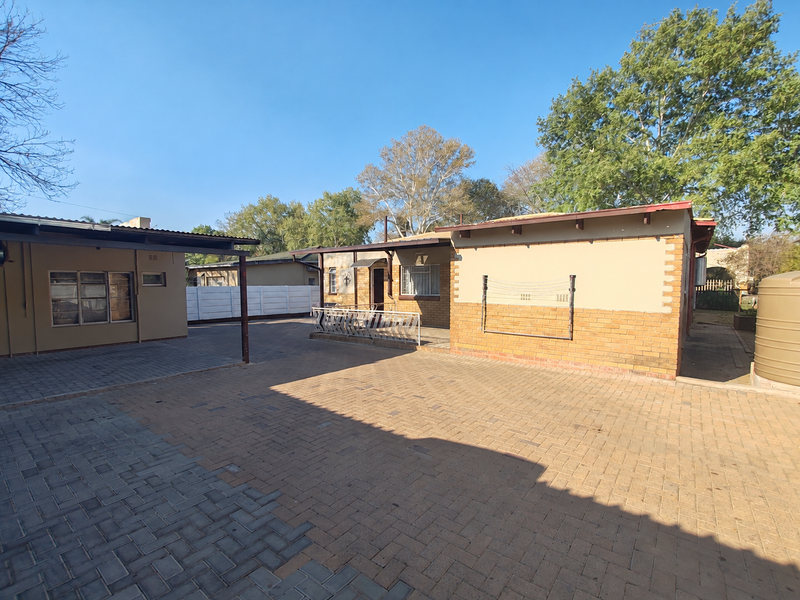Rear exterior view of the property featuring a large paved courtyard, covered patio area, brick facade, and a water storage tank.