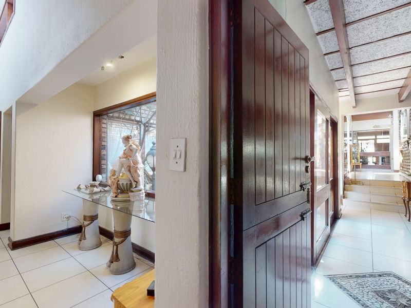 Spacious hallway featuring tiled flooring, exposed beam ceilings, and a brick feature wall, connecting multiple areas of the home with a traditional aesthetic.