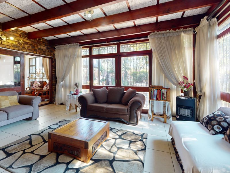 Spacious living room featuring exposed timber ceiling beams, a rustic brick feature wall, and large timber-framed windows providing ample natural light.
