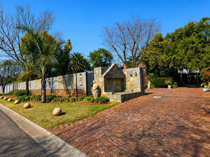 Front exterior view featuring a brick paved driveway, stone-clad boundary wall, and a decorative stone fountain feature at the property entrance.