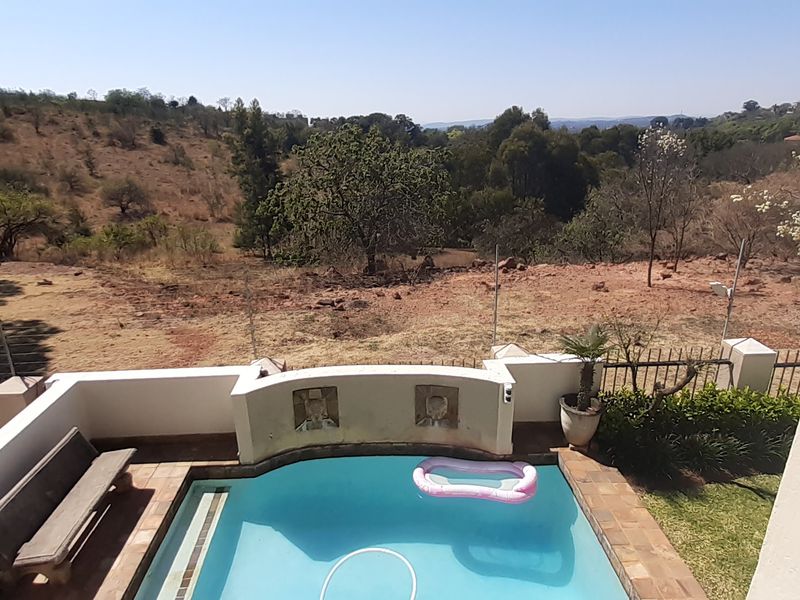 An elevated view of a swimming pool area featuring a tiled surround and perimeter fencing, overlooking a natural landscape.