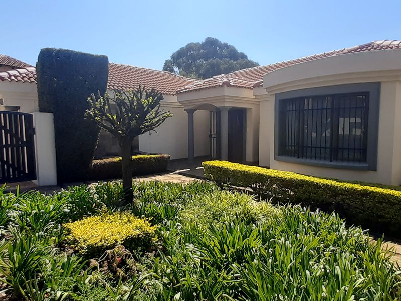 Front elevation of a well-maintained house featuring a terracotta tiled roof, secure entrance gate, and established landscaped garden.