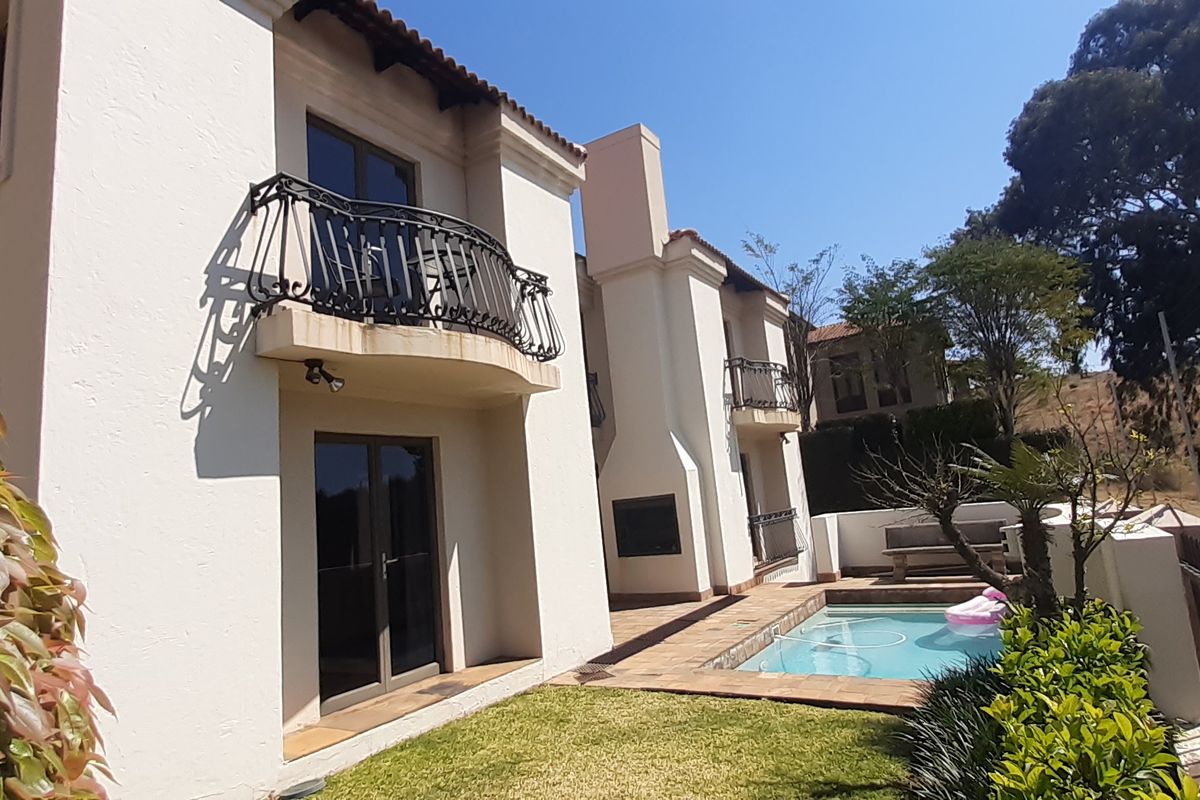 Rear exterior view featuring a swimming pool, tiled patio area, built-in outdoor fireplace, and upper-level balconies with wrought iron railings.