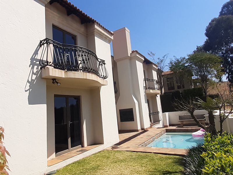 Rear exterior view featuring a swimming pool, tiled patio area, built-in outdoor fireplace, and upper-level balconies with wrought iron railings.