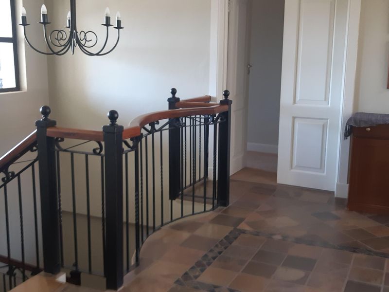 A well-maintained upper hallway featuring decorative wrought iron staircase railings with a wooden handrail and classic tiled flooring.