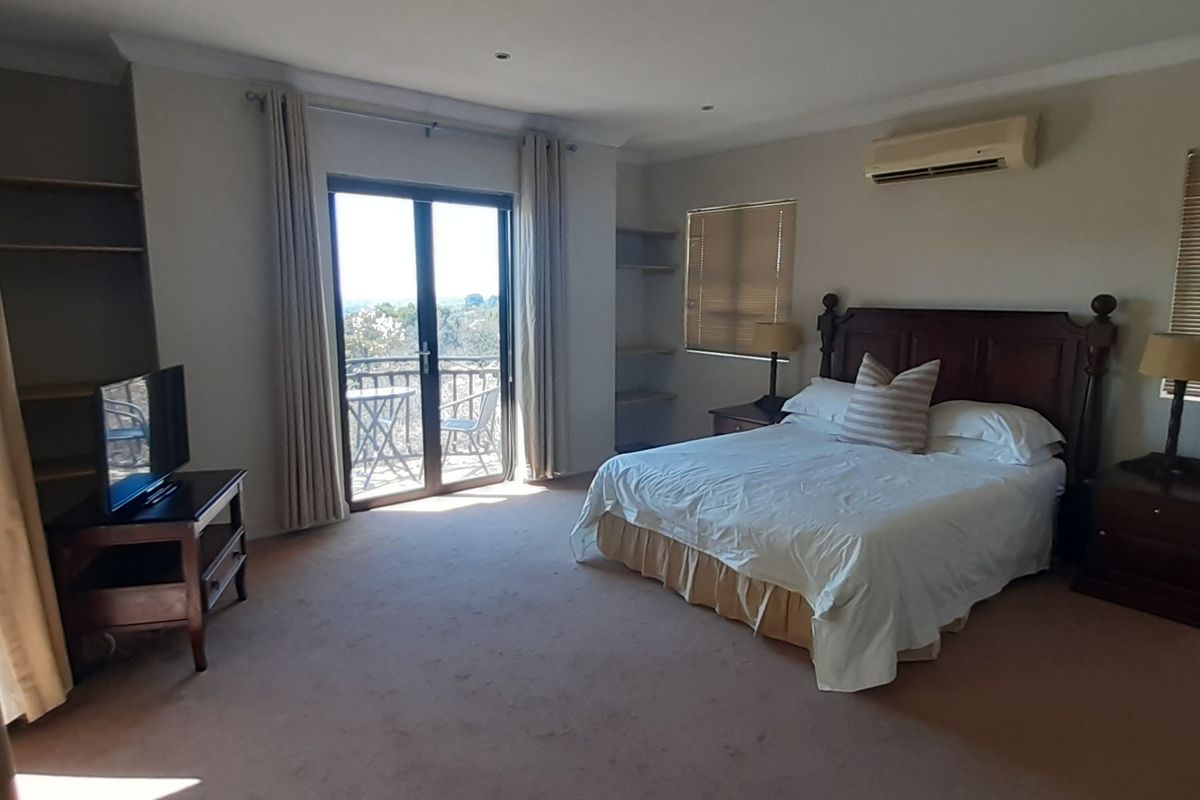 Spacious bedroom featuring built-in shelving, split-system air conditioning, and a sliding glass door leading to a private balcony with scenic views.