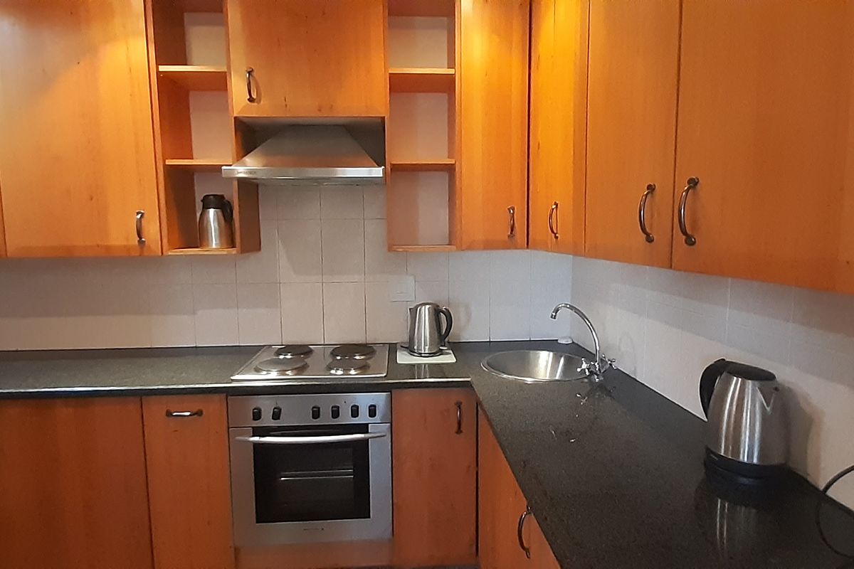 A functional kitchen featuring warm-toned wooden cabinetry, dark granite countertops, a built-in oven, electric hob, and a tiled backsplash.