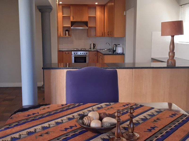 Open plan kitchen and dining area featuring wooden cabinetry, granite countertops, built-in oven, and structural columns, creating a functional living space.