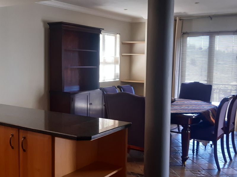 Open-plan living and dining area featuring tiled floors, a granite-topped kitchen island, and built-in shelving, creating a functional and connected living space.