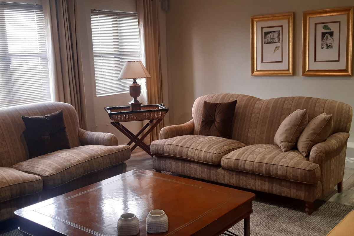 A comfortable living room featuring laminate flooring, venetian blinds, and a wall-mounted air conditioning unit.