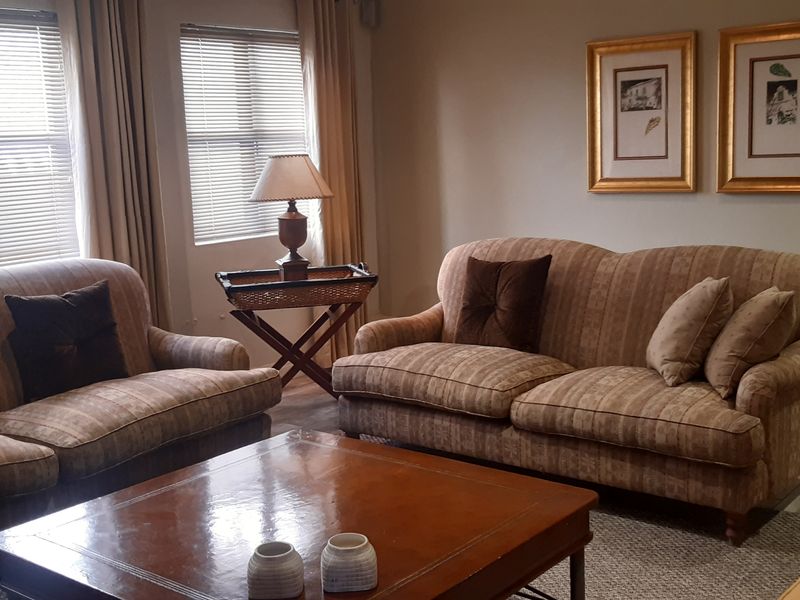 A comfortable living room featuring laminate flooring, venetian blinds, and a wall-mounted air conditioning unit.