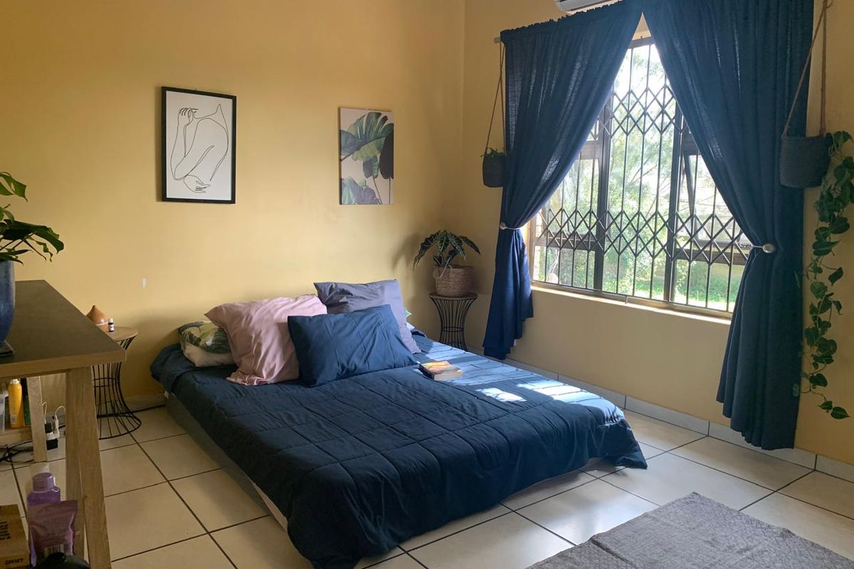 A bedroom featuring tiled flooring, a security gate on the window, and a wall-mounted air conditioning unit.