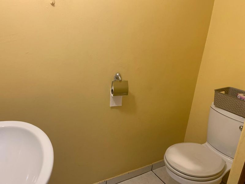 A compact bathroom featuring a standard toilet, washbasin, and tiled flooring, currently showing signs of wear on the wall surfaces.