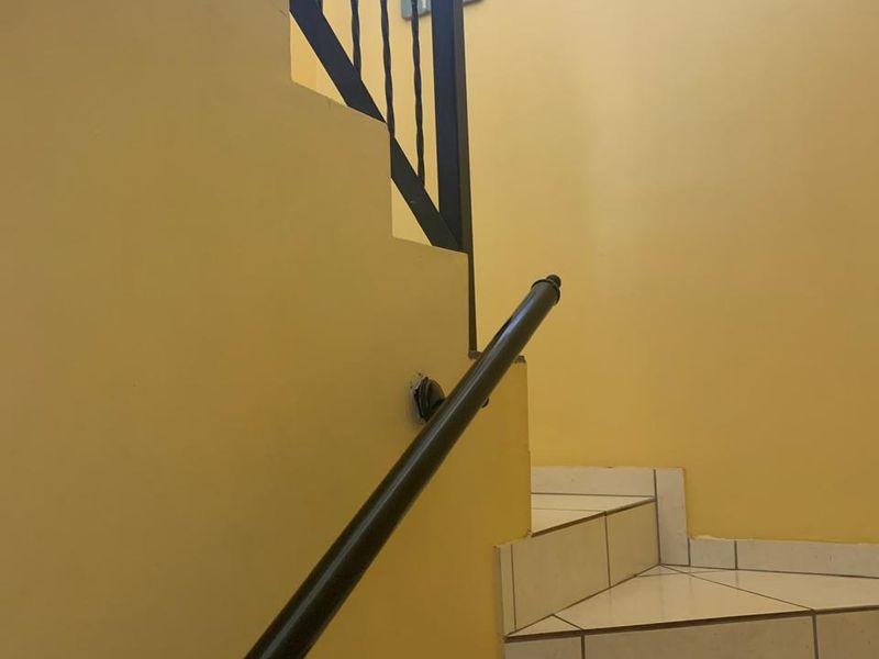 A staircase featuring tiled steps and a wrought iron balustrade with a wall-mounted handrail, providing access between levels in the townhouse.