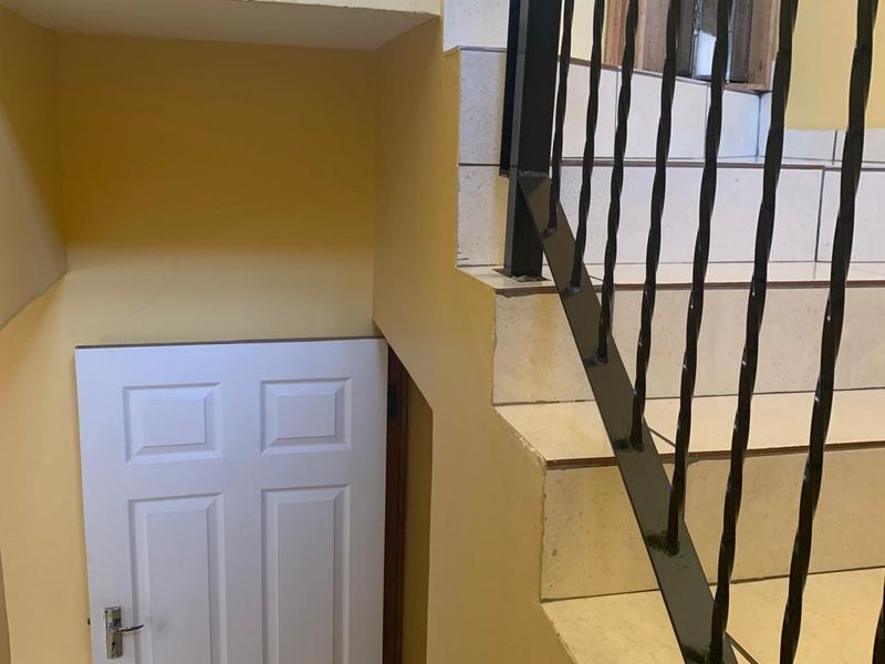 A tiled staircase featuring a wrought iron balustrade leading to an internal door in a townhouse hallway.