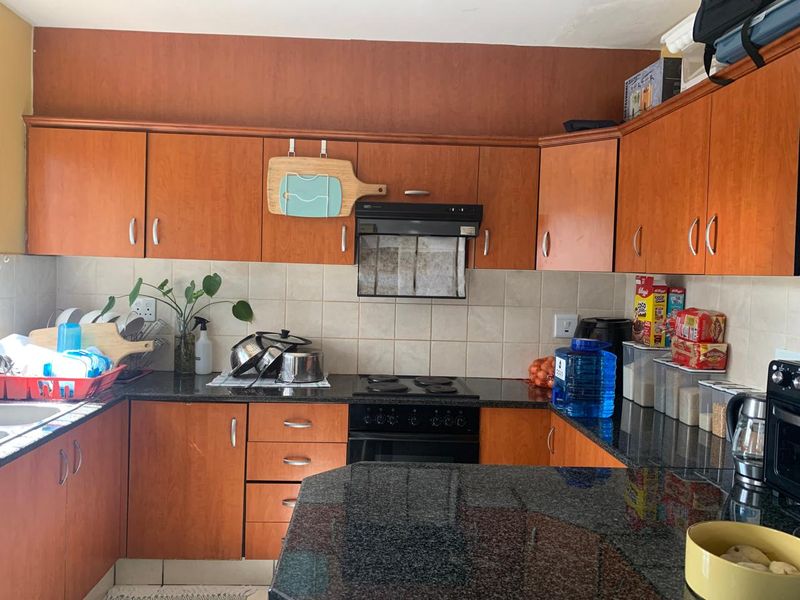 A functional kitchen featuring wood-finish cabinetry, granite countertops, and a tiled backsplash, equipped with a built-in oven, hob, and extractor fan.
