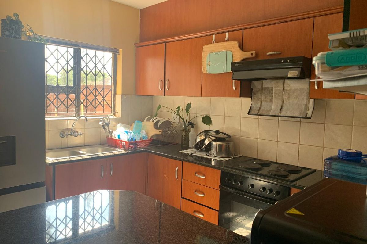 A functional kitchen featuring wooden cabinetry, granite countertops, a built-in oven with hob, and a tiled backsplash with a window overlooking the exterior.