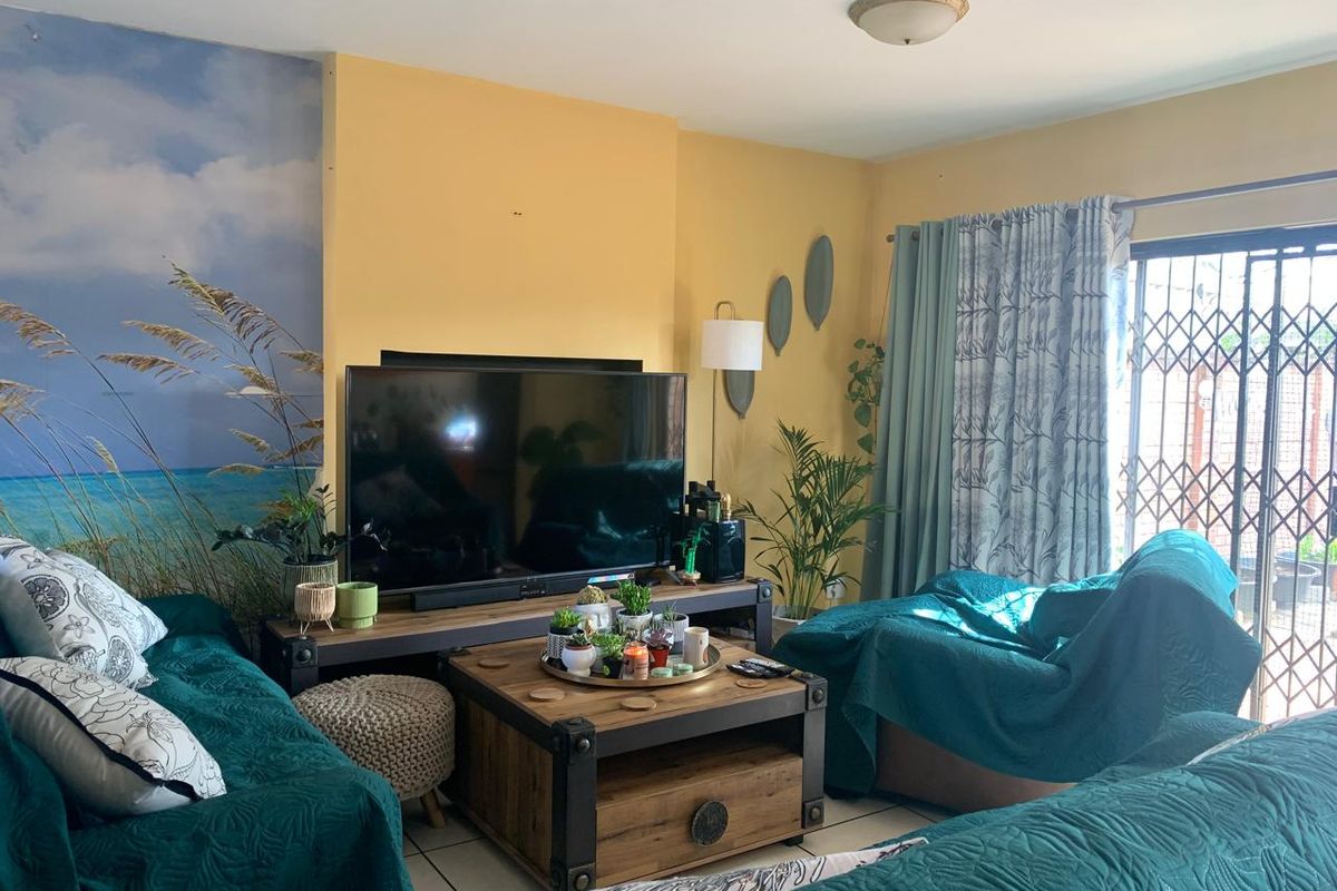 A comfortable living room featuring tiled flooring and a sliding glass door with a security gate, providing access to the outdoor area.