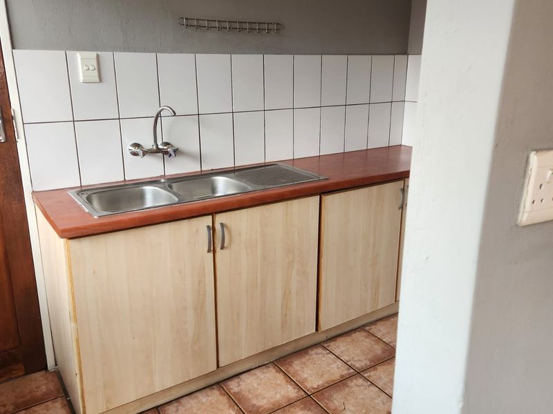 A compact kitchen area featuring a double sink, laminate countertop, base cabinetry, and tiled backsplash with durable floor tiles.
