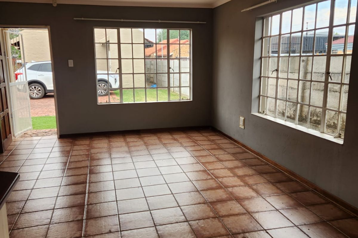 An empty living room featuring tiled flooring, large grid-pattern windows, and direct access to the exterior, offering a blank canvas for interior design.